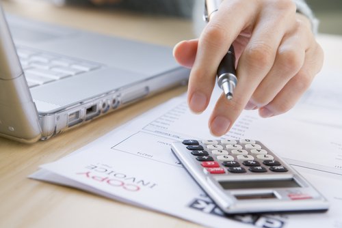 Person holding pen and entering into a calculator on a desk