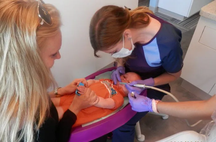 Dr. Felton cleaning toddler's teeth while mother holds toddler's hands